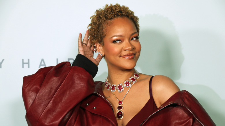 Rihanna posing at an event with short hair wearing a red leather outfit with a red statement necklace.