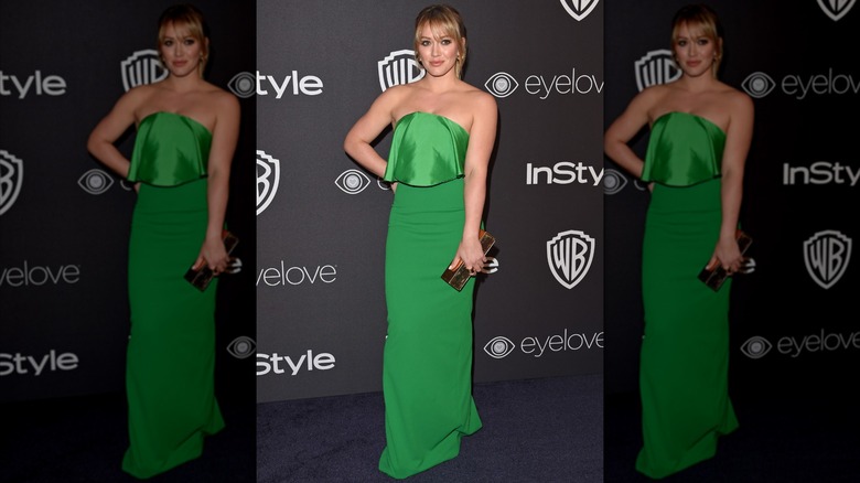 Hilary Duff posing at an event with her hand on her hip wearing an emerald-green strapless dress.