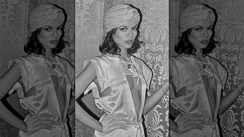 Bianca Jagger posing in a black and white photoshoot wearing a turban hat and eclectic outfit.