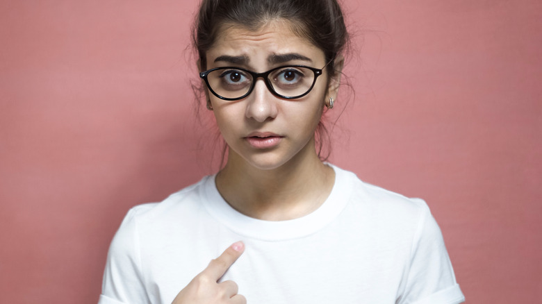 Woman pointing at herself, looking doubtful