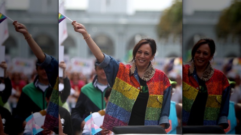 Kamala Harris waving a flag at Pride while in a rainbow vest and denim shirt