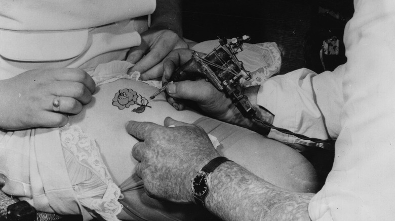 tattooist inking flower on woman