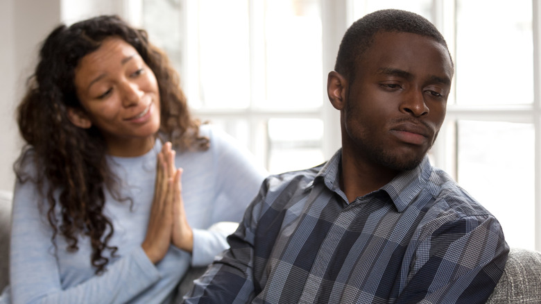 African American man and woman on couch, woman making a pleading gesture with hands and man turning away sulkily