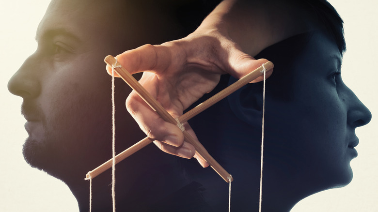 Man and woman in profile with superimposed hand controlling puppet strings