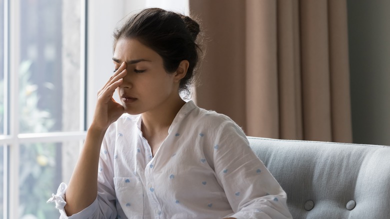 Depressed woman sitting at window with face in hands