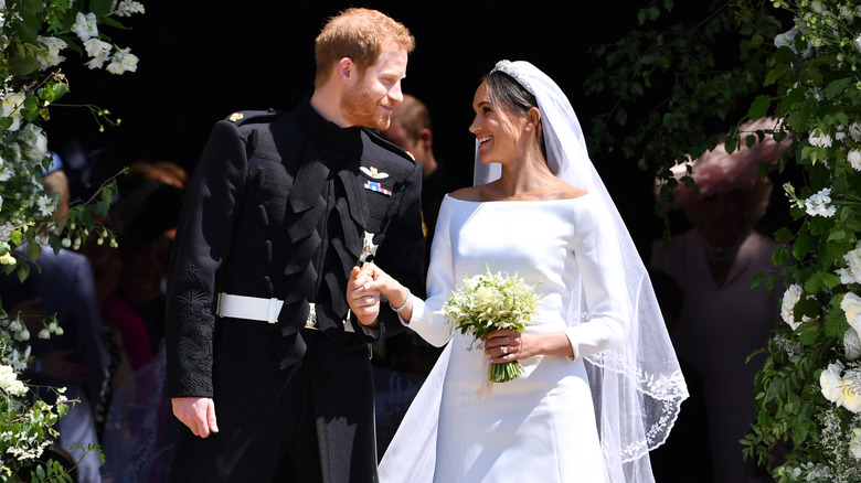 Meghan Markle in her expensive wedding dress and Prince Harry holding hands at their wedding
