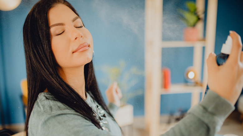 A woman spraying setting spray on her makeup
