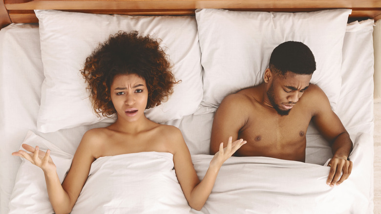 woman shrugging in bed man looking sad
