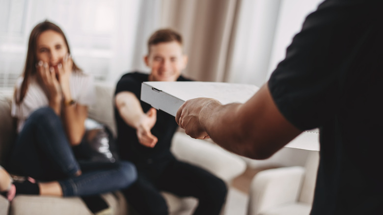 Person handing pizza to friends