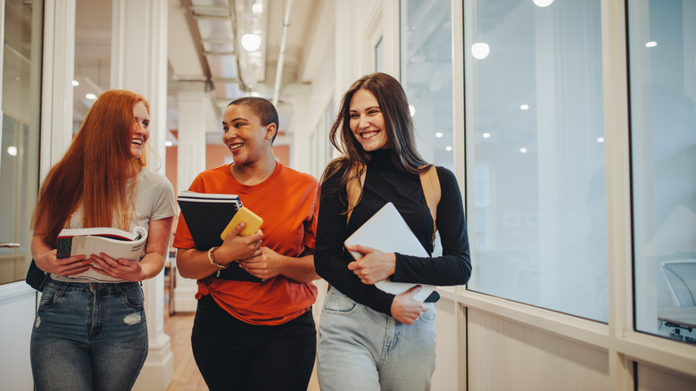 Women smiling and holding books while walking down a hallway