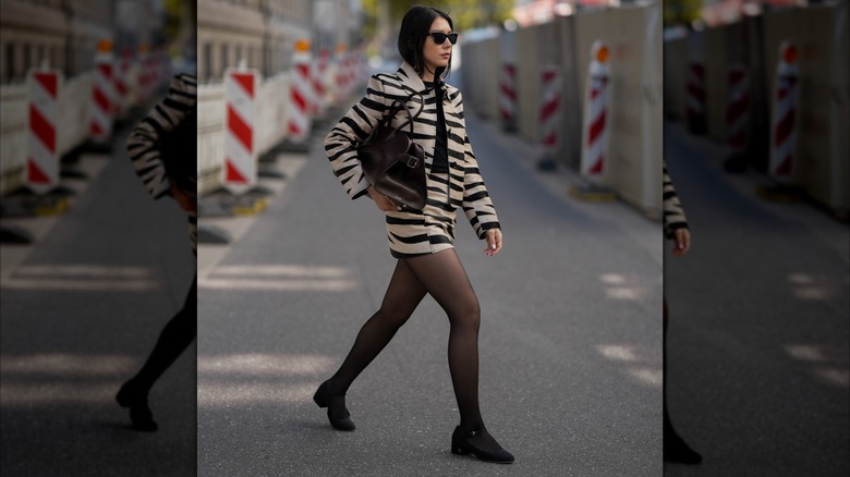 A woman wearing black Mary Janes with white lining and a white skirt on a walk