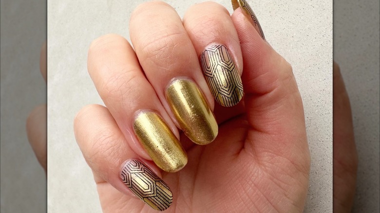 An art-deco manicure with gold nails and intricate black line work