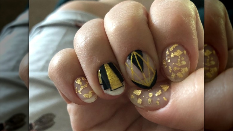 An art-deco manicure with black-and-gold nails featuring gold flakes