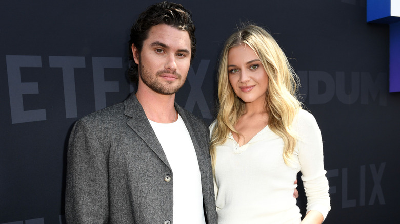 Chase Stokes and Kelsea Ballerini stand side by side on a red carpet