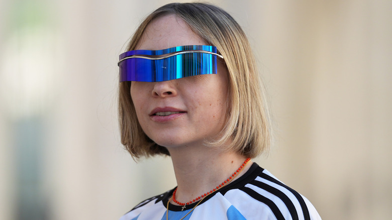 A person wearing reflective sunglasses and a blunt blond bob
