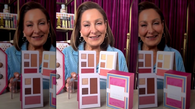 Laura Geller posing with makeup palettes in front of her.