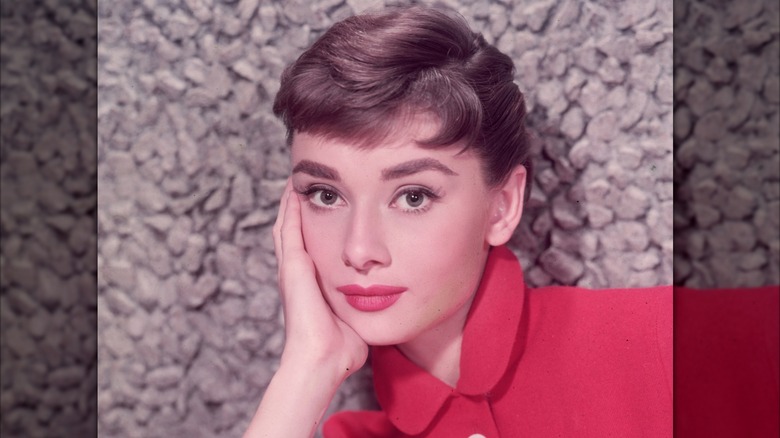 Audrey Hepburn posing with her head in her hand wearing a red top