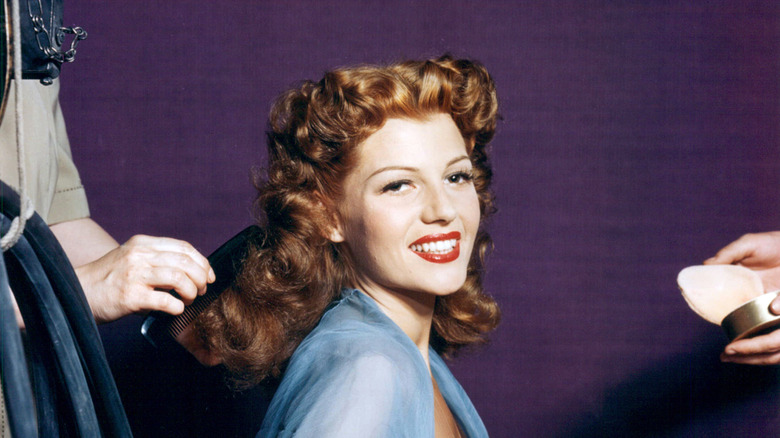 Rita Hayworth getting her hair combed wearing a blue sheer top.
