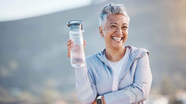 An older woman drinking water out of a glass bottle