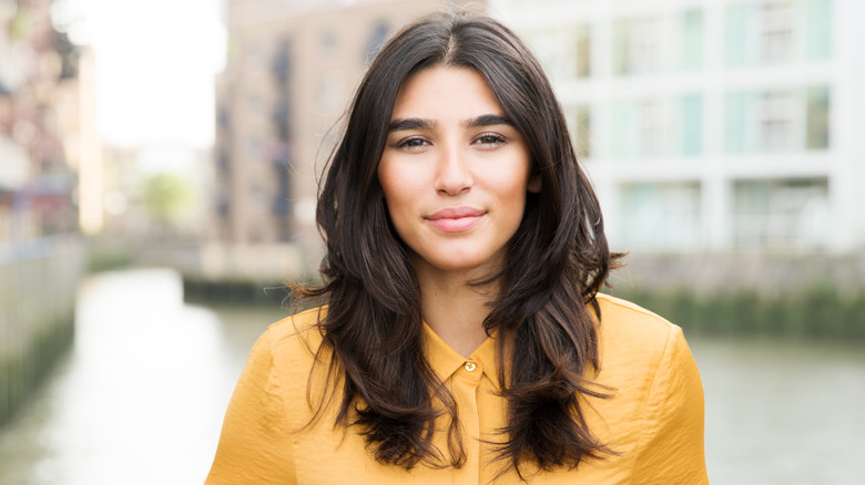 A woman with dark hair and textured relaxed waves posing in front of river