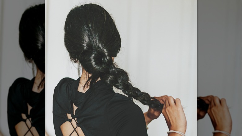 A woman braiding her long hair black behind her.