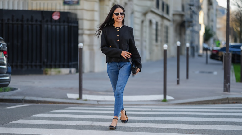 A woman with skinny jeans and a black top walking across a crosswalk