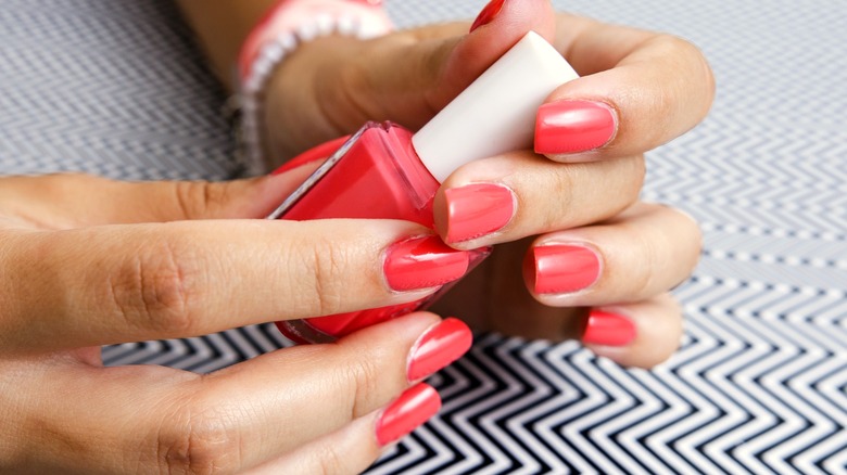 Dark coral manicure holding nail polish