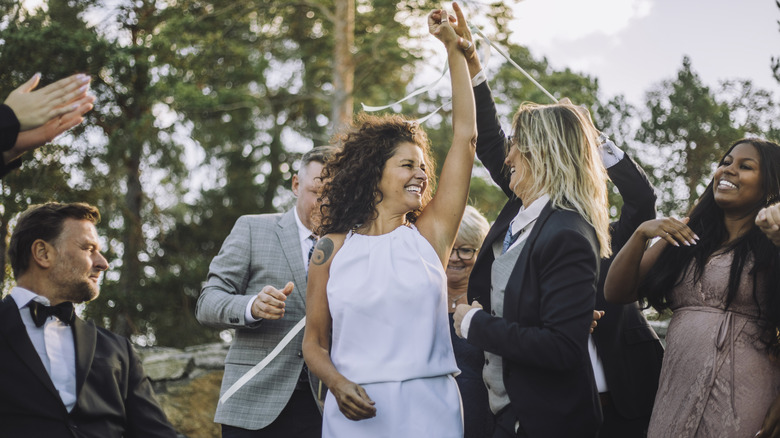 Two newlyweds, one in a white outfit and one in a suit, celebrating with family and friends at their wedding