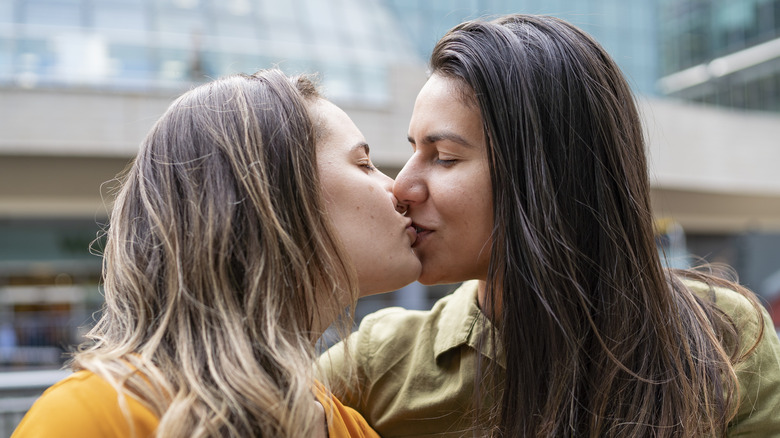 Two women sharing a closed-mouth kiss.