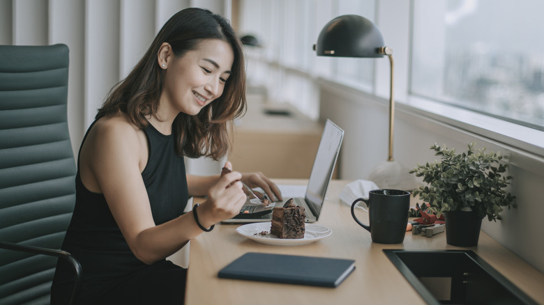 Woman eating cake at desk