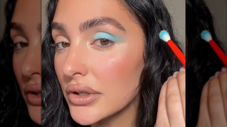 Still image from a makeup tutorial of a woman applying bright blue eyeshadow.
