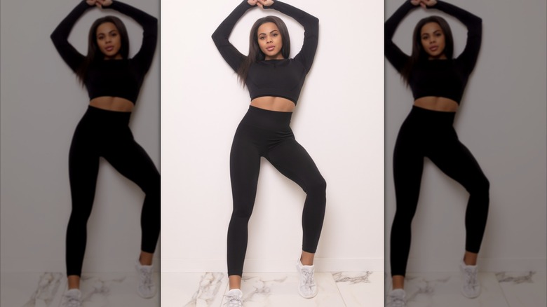 Woman poses while wearing black crop top and high waisted leggings while stretching