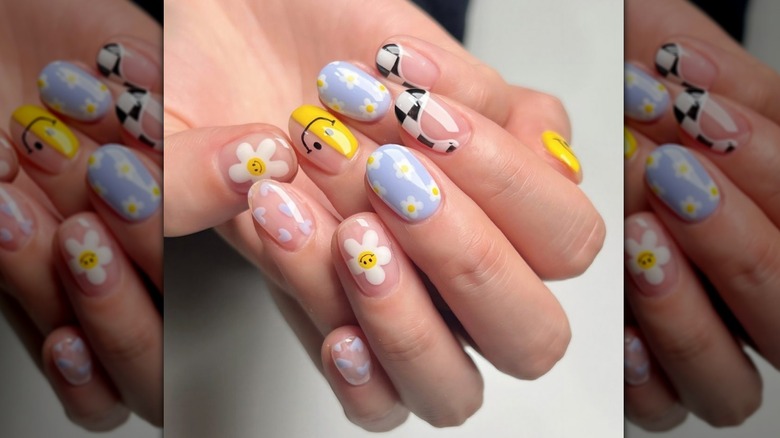 Close up image of a manicure featuring flowers, smiley faces, and swirls.