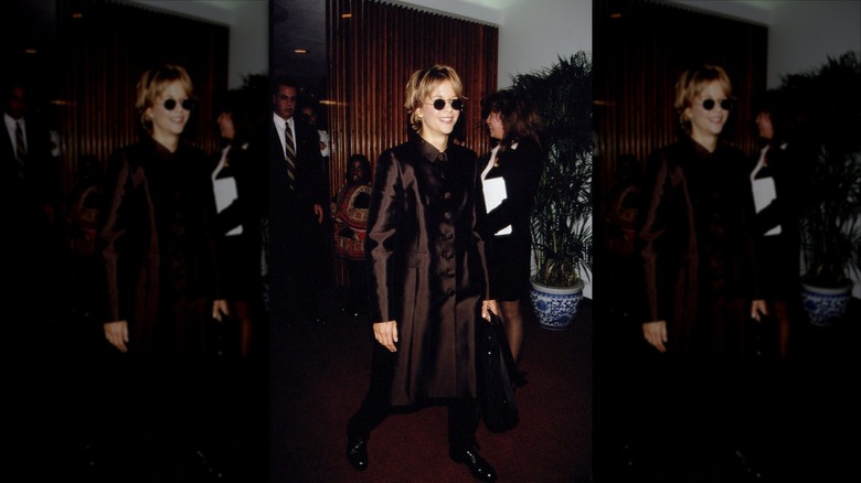 Meg Ryan smiling and wearing a brown coatdress and sunglasses.