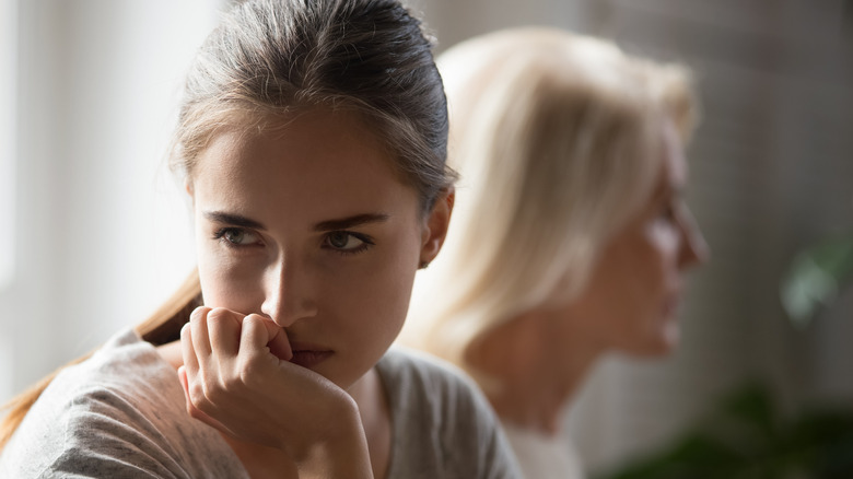 Young woman with depressed expression turning away from older woman in background
