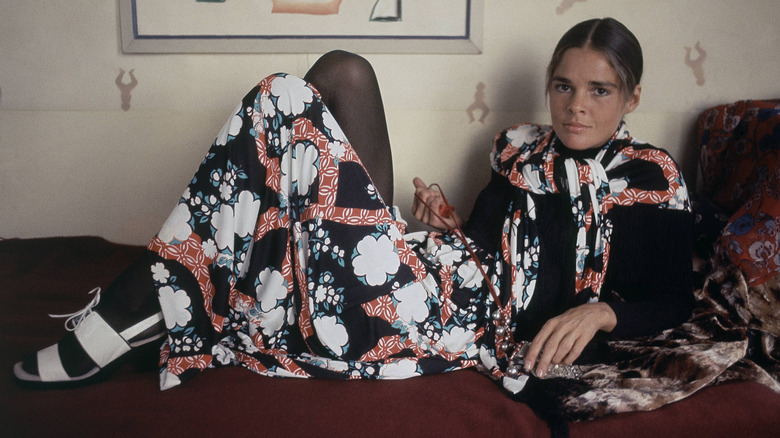 Actress Ali MacGraw lounging on a couch wearing an Asian-inspired outfit with white shoes.