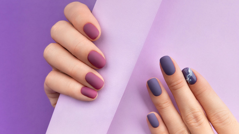 Two hands showing off different manicures in shades of purple