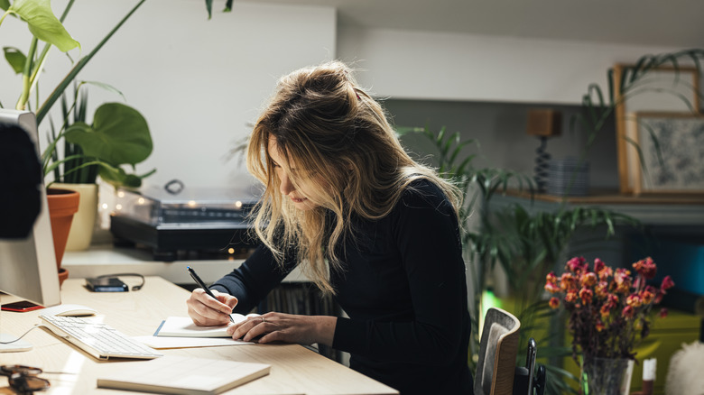 Woman sitting, writing at desk