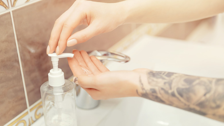 Tattooed person dispensing soap as they wash their hands