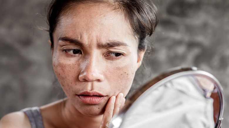 Woman looks concerned into mirror
