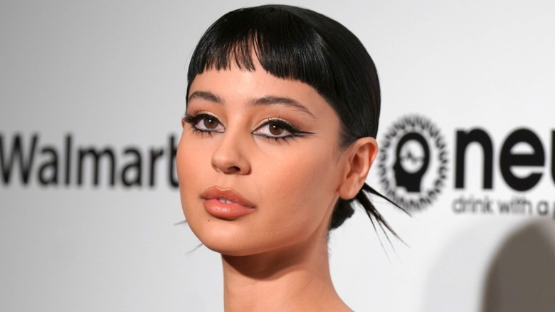 Close-up shot of Alexa Demie at an event in 2020. She is wearing a dramatic eye look with thick black eyeliner, and her hair is slicked back into a bun - her microbangs are left out.