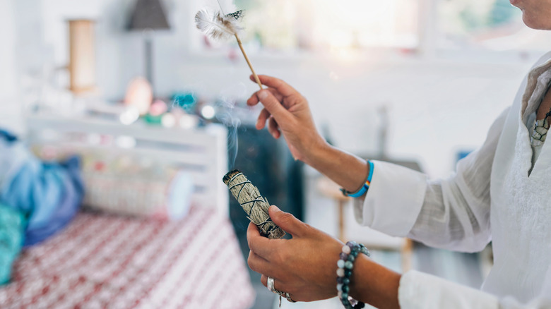 Woman wafting the smoke from a burning smudge stick with a white feather.