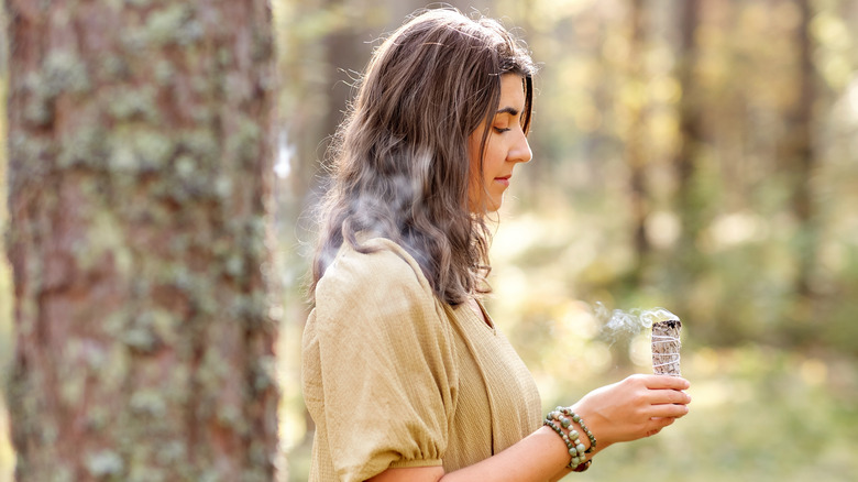 Woman in the woods holding a smoking sage stick.