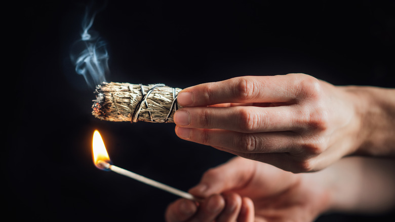 Burning a sage bundle with a long lit match.