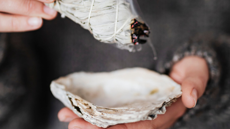 Woman holding a shell under a burning sage bundle