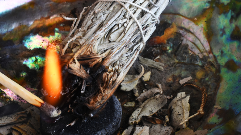 A lit match lighting the ends of a sage bundle.