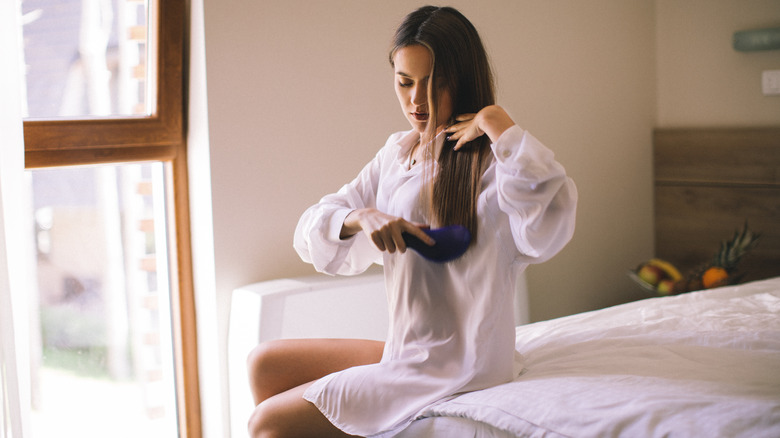 woman brushing hair on bed