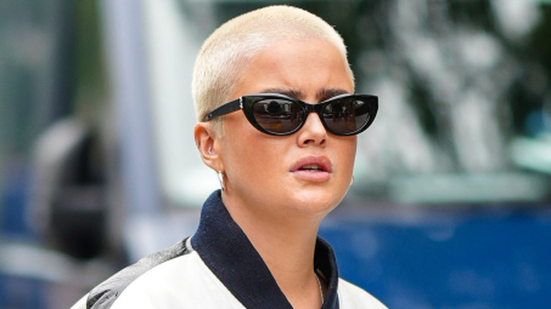 A person with a buzzcut wearing sunglasses and a jacket