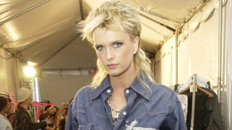 A person with a blond shaven mullet wearing a denim jacket