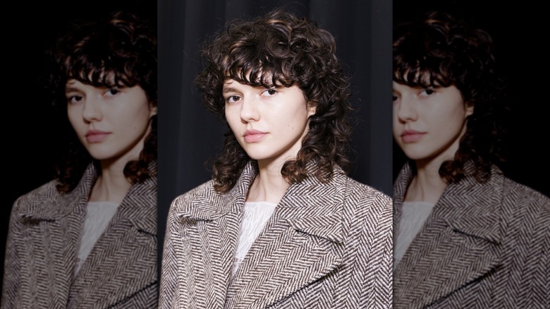 A person with a curly wolf cut wearing a blazer